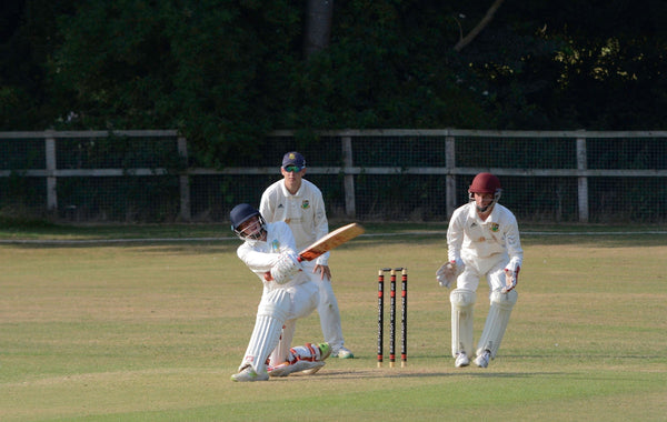 2 men playing cricket on green grass field during daytime