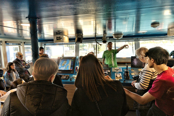 People gathered in a ship's bridge listening to a guide.