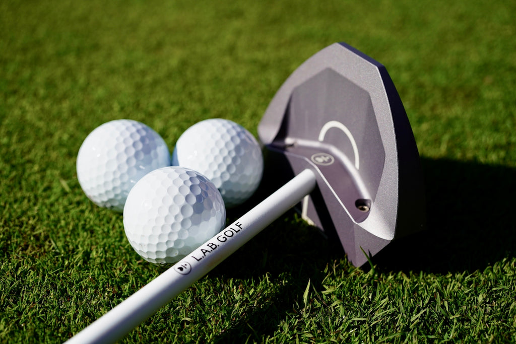Three golf balls and a putter on green grass.
